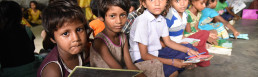 Group of underprivileged children sitting in a classroom, holding books and slates, indicating the importance of education.